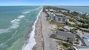 An aerial view of a coastal area with a beach, buildings, and a clear view of the ocean.