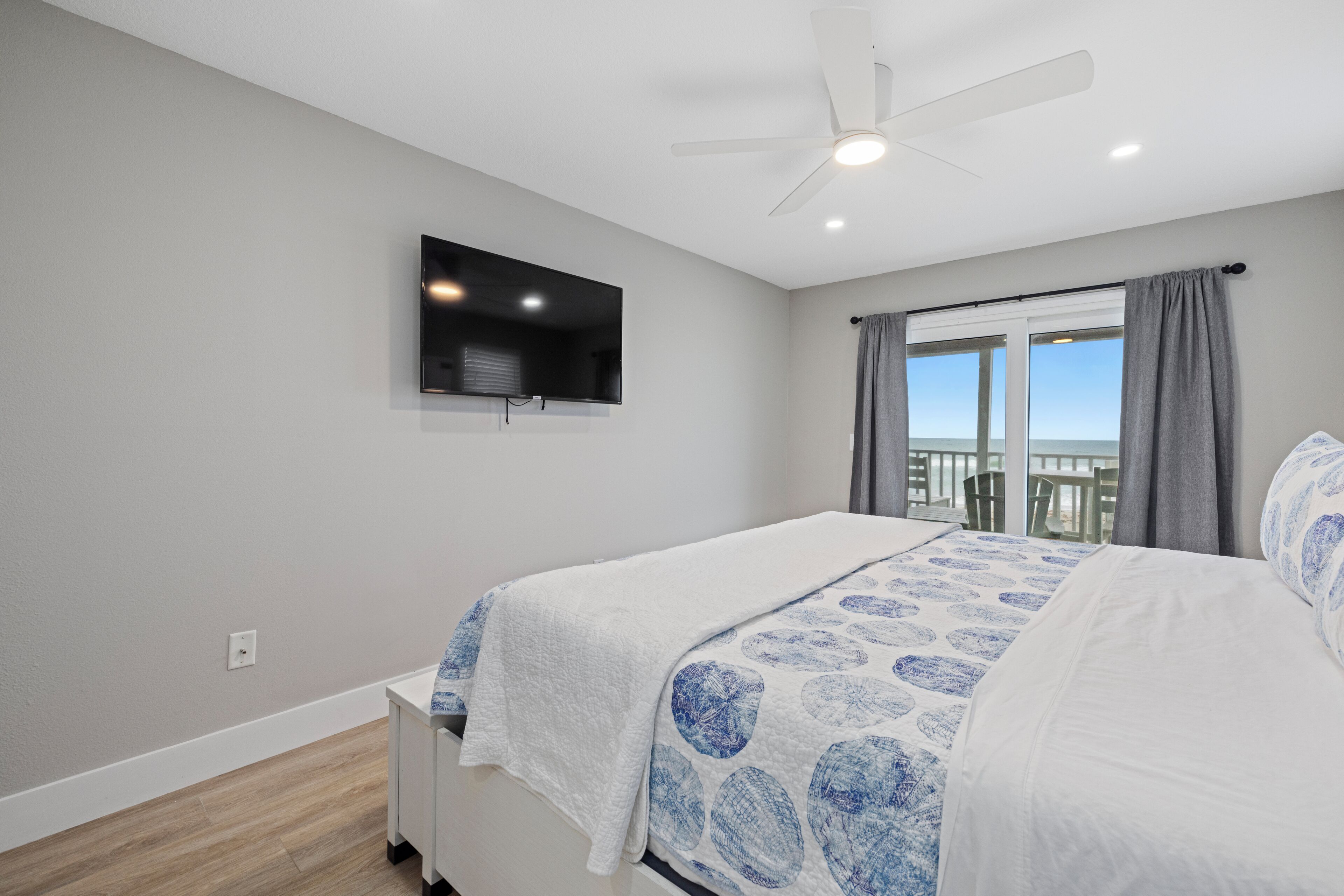 A bedroom with a bed, a ceiling fan, a TV mounted on the wall, and a window with curtains.