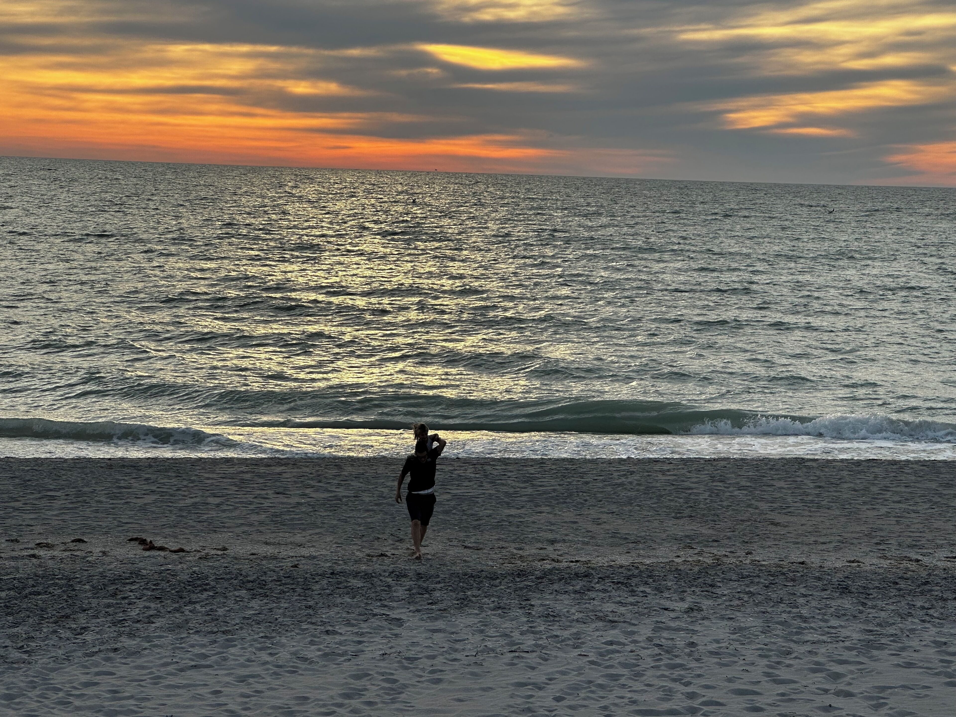 Escena de playa con una persona de pie mirando al océano durante el atardecer.