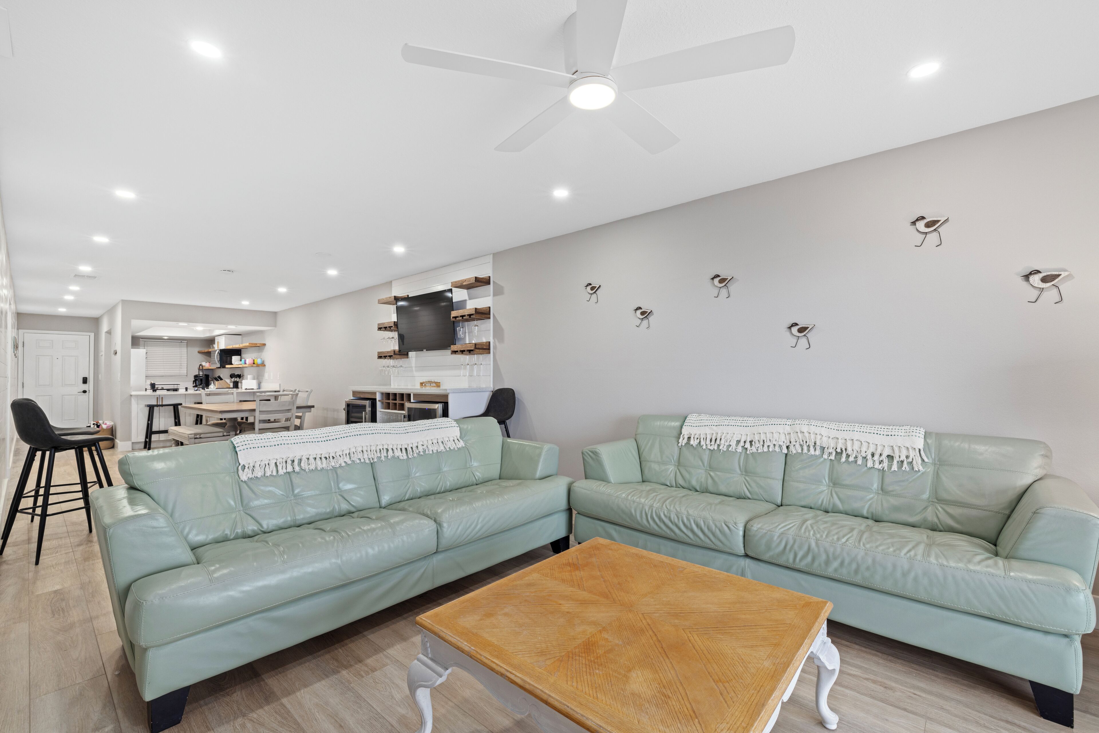 Un salon moderne avec deux canapés en cuir vert clair, une table basse en bois et un ventilateur de plafond.