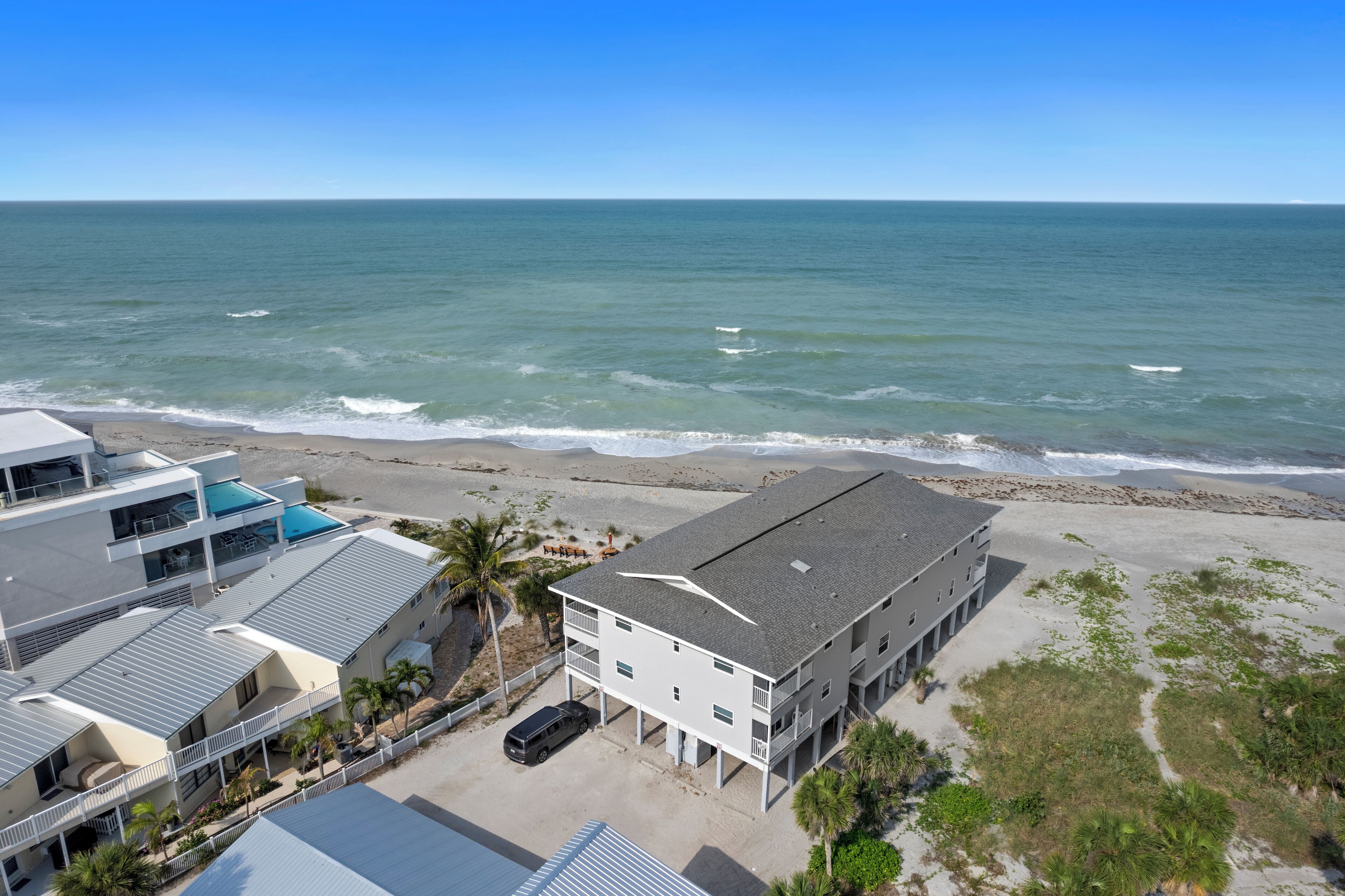 A beachfront hotel with multiple buildings, a swimming pool, and a view of the ocean.