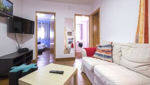 Ein Wohnzimmer mit Fernseher, Sofa, Couchtisch und einem Bett im Hintergrund.