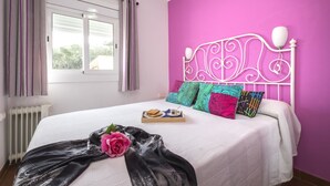Ein Schlafzimmer mit Bett, einem Fenster mit Vorhängen, einem Heizkörper und einer rosa Wand.