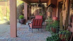 A covered patio area with brick flooring, a red striped sofa, and potted plants. - The Camelback Ranch in Litchfield Park - Amazing Backyard | Refreshing Pool (Litchfield Park)