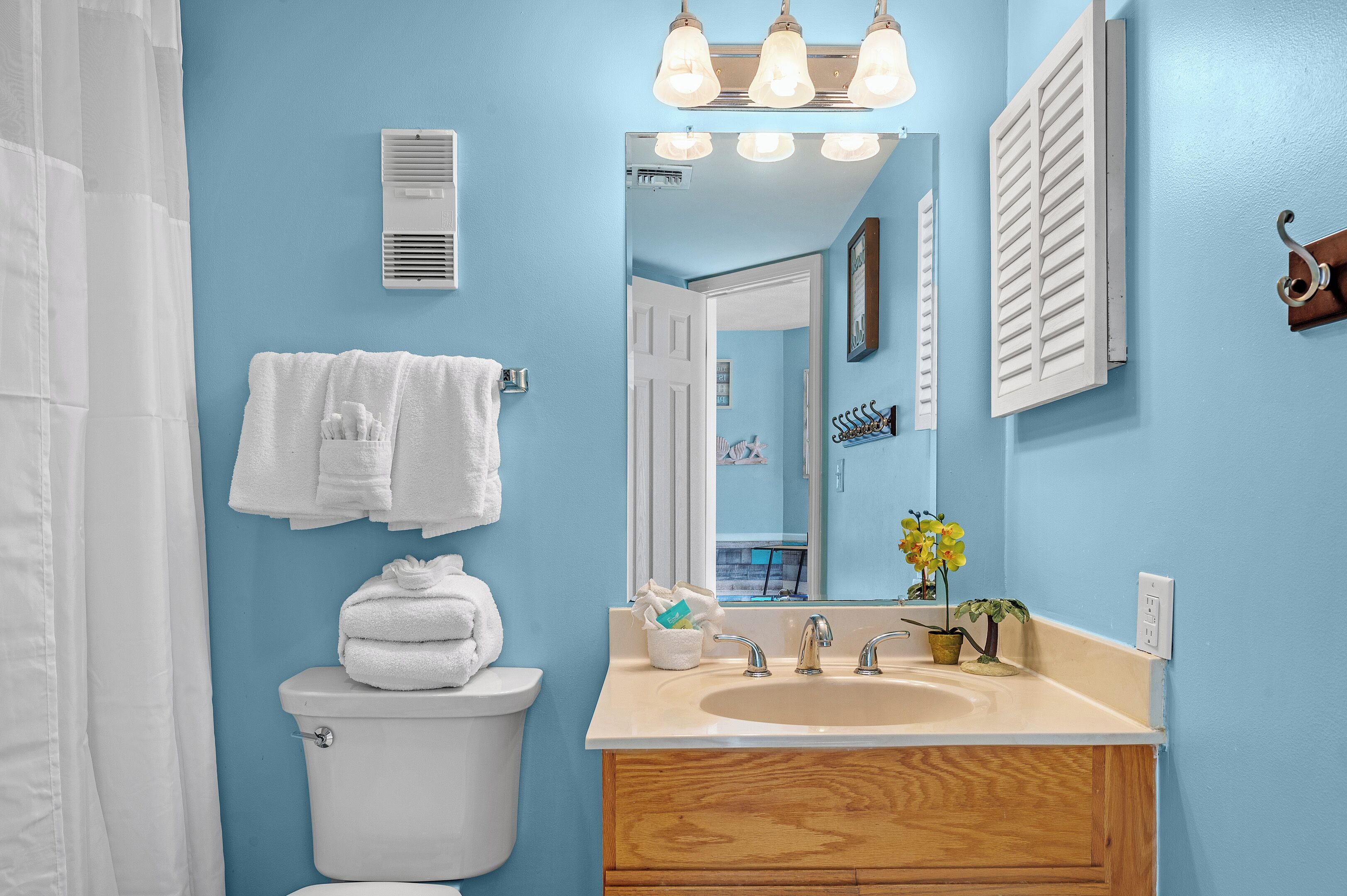 Une salle de bain avec des toilettes blanches, un lavabo avec un meuble-vasque en bois, un miroir et un porte-serviettes.