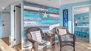 Ein Zimmer mit Stranddekoration, einschließlich einer Wand mit einem Stern und Schildern mit den Aufschriften 'WELCOME TO BEACH' und 'BEACH RULES'. Es gibt Korbstühle und einen kleinen Tisch mit einer Lampe.