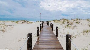Ein hölzerner Weg führt zum Strand, begleitet von Dünen auf beiden Seiten.