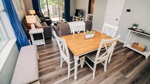 A cozy living room with a wooden dining table, white chairs, a sofa, and a bench.