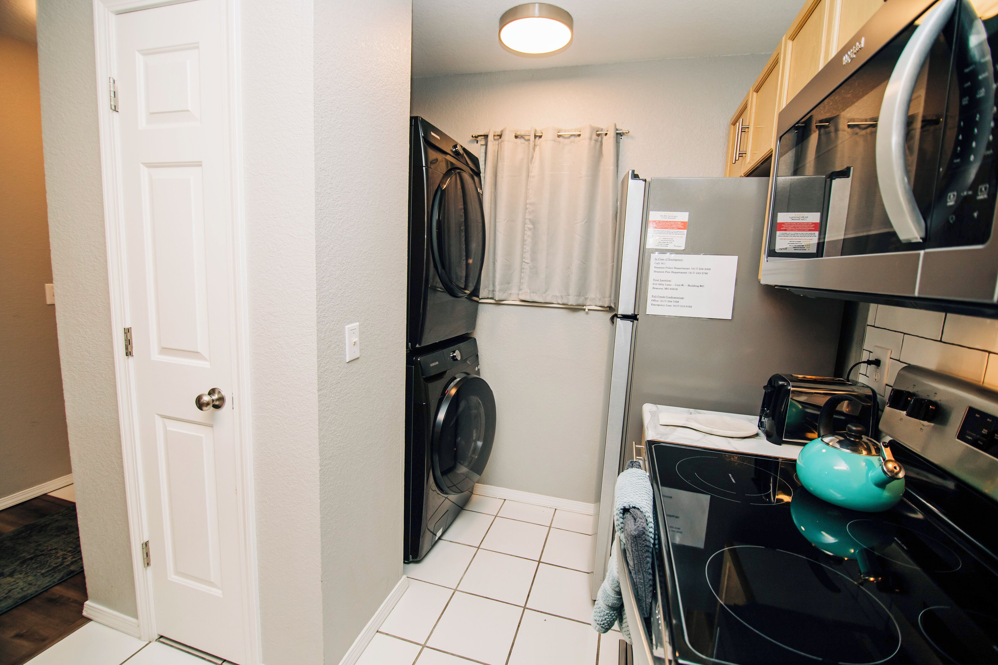 A compact kitchen with a washing machine, a refrigerator, and a microwave.