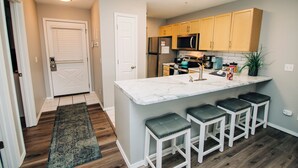 A modern kitchen with a marble island, bar stools, wooden cabinets, stainless steel appliances, and a small potted plant.