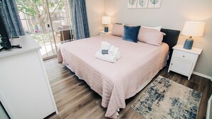 A bedroom with a bed, two bedside tables, a desk, and a view of the outdoors.