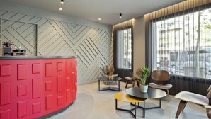 A modern reception area with a red counter, geometric wall design, and a seating area with round tables and chairs. - Hotel Climent (Barcelona)