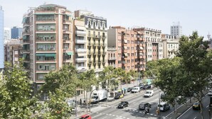 A multi-story residential building with balconies, a street view with parked cars, and a clear sky. - Hotel Climent (Barcelona)