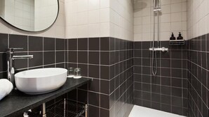 A modern bathroom with a round mirror, a white sink, and a shower. - Hotel Climent (Barcelona)