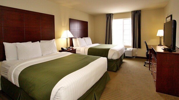 Habitación de hotel con dos camas, un escritorio, un televisor y una ventana con cortinas.