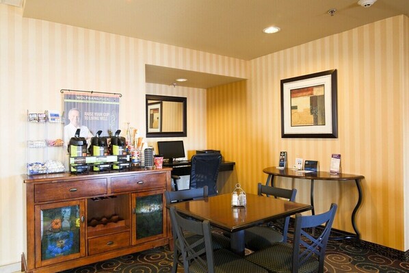 A hotel room with a wooden cabinet, a dining table, and chairs. There is a poster on the wall and a framed picture above the table.