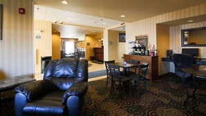 Un vestíbulo de hotel con un sillón de cuero, una zona de bar y una mesa de comedor con sillas.