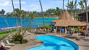 A swimming pool with a dolphin, surrounded by lounge chairs and a beach view.