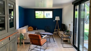 A modern living room with a blue accent wall, a sofa, a rocking chair, and a dining area with a table and chairs. - Our doll's house 2 steps from the shops and 800m from the beach. (Trébeurden)
