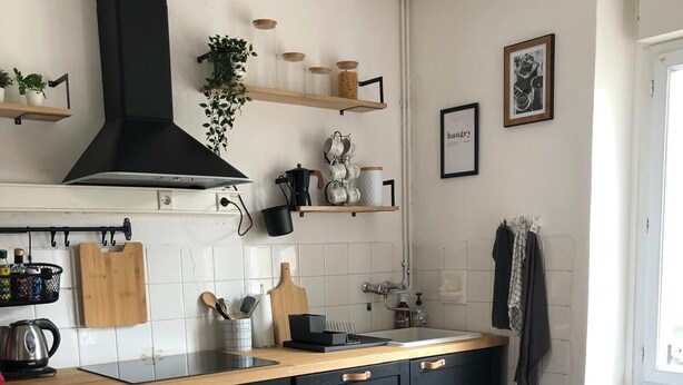 A modern kitchen with black cabinets, a wooden dining table set for a meal, and a black range hood above the stove. - Our doll's house 2 steps from the shops and 800m from the beach. (Trébeurden)