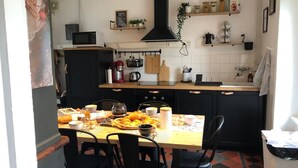 A kitchen with a dining table set for four, a black stove, a microwave, and various kitchen utensils and appliances. - Our doll's house 2 steps from the shops and 800m from the beach. (Trébeurden)