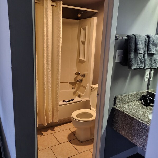 Een badkamer met toilet, bad en douchegordijn. Er is een handdoekhouder met handdoeken aan de muur.