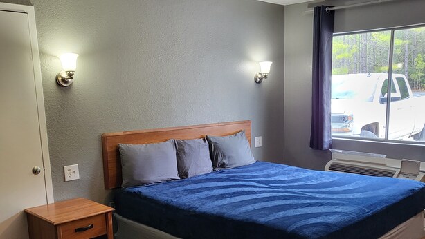 Un dormitorio con una cama de madera, una mesita de noche, un ventanal con vistas a un camión y un calentador fijado a la pared.