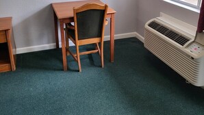 Habitación de esquina con un escritorio de madera, una silla, una ventana y un equipo de aire acondicionado.