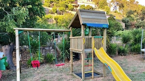 A wooden play structure with a slide and swings in a grassy area. - Quinta da Villa - House of Wines (Cascais)