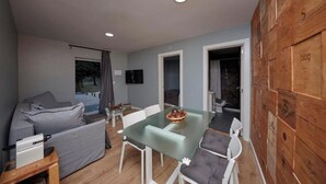 A modern living room with a glass-top dining table, grey sofa, and a wooden accent wall. - Quinta da Villa - House of Wines (Cascais)