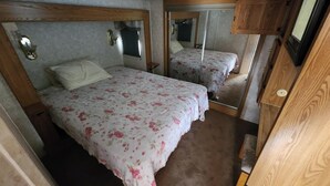 A compact RV bedroom with two beds, wooden headboards, and a mirror. - 1-bedroom 5th Wheel in Parker w/ WiFi, AC. Enjoy a cozy stay in Cienega Springs (Parker)