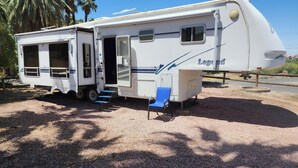 A white RV with a side door open, a blue chair, and a small window. - 1-bedroom 5th Wheel in Parker w/ WiFi, AC. Enjoy a cozy stay in Cienega Springs (Parker)