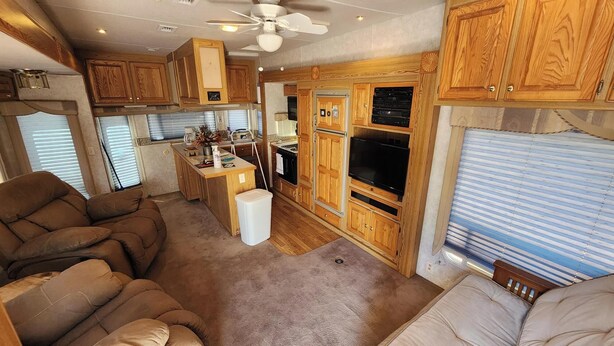 A compact RV interior with wooden cabinetry, a kitchenette, a seating area with two sofas, and a ceiling fan. - 1-bedroom 5th Wheel in Parker w/ WiFi, AC. Enjoy a cozy stay in Cienega Springs (Parker)