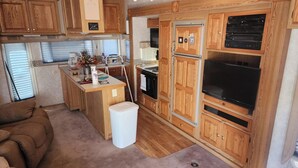 A compact RV kitchen with wooden cabinets, a stove, a refrigerator, and a TV. - 1-bedroom 5th Wheel in Parker w/ WiFi, AC. Enjoy a cozy stay in Cienega Springs (Parker)