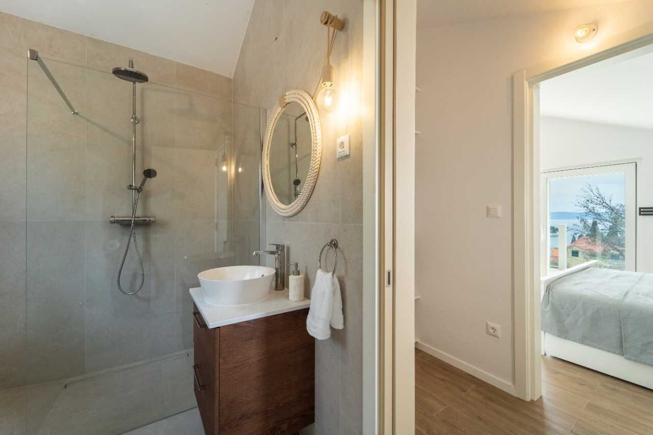 Ein modernes Badezimmer mit einer gläsernen Duschkabine, einem weißen Waschbecken und einem Holz-Waschtisch.