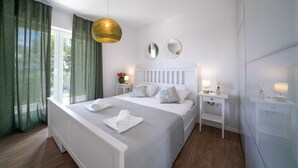 Et moderne hotelværelse med en stor seng, to sengeborde, en hængende lampe og udsigt til det fri.
