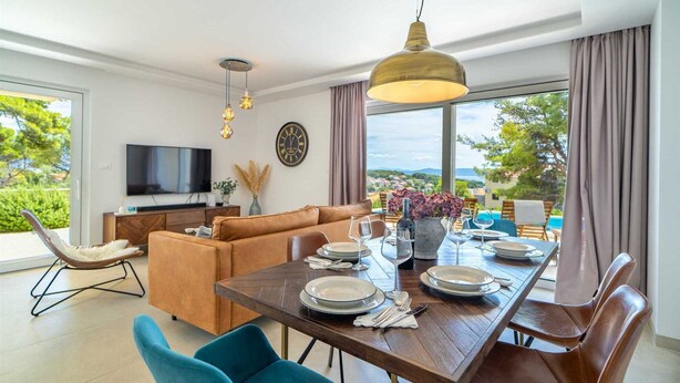 En moderne stue med sofa, spisebord til fire personer og fjernsyn på væggen.