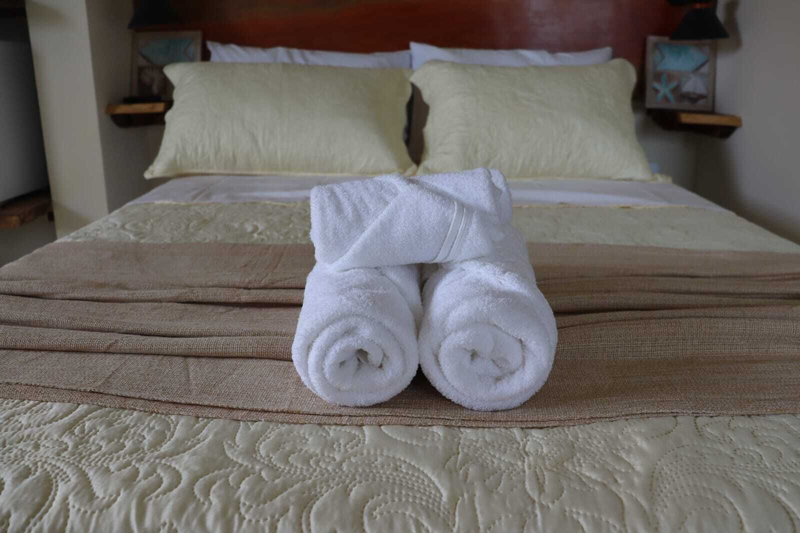 A neatly made bed with two rolled white towels placed on top, a beige bedspread, and matching pillows.