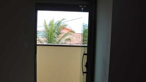 Habitación de hotel con cama, alfombra estampada y puerta corredera que da a un balcón con vistas a edificios y palmeras.