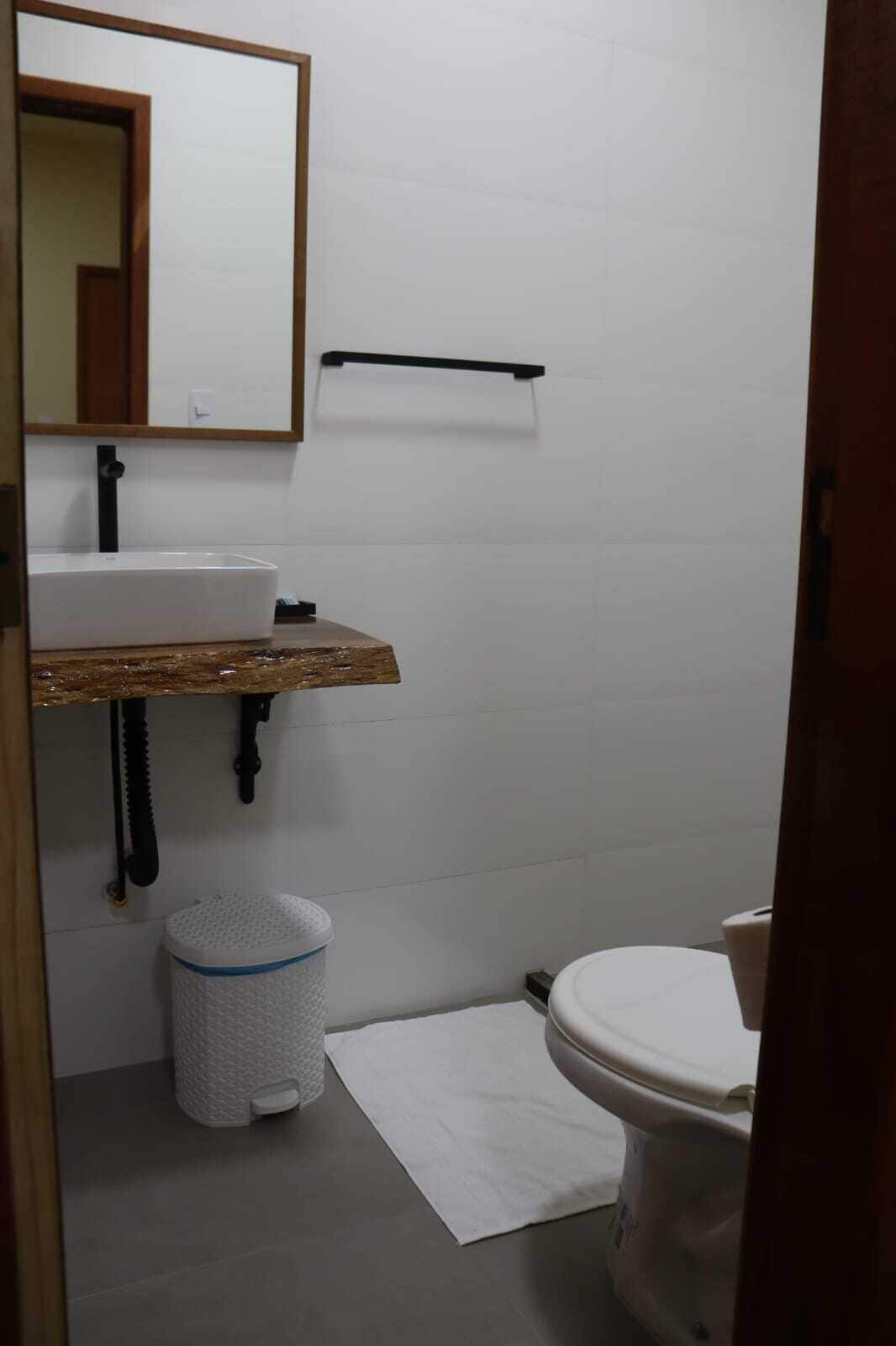 Um banheiro pequeno com pia branca, espelho, vaso sanitário e lixeira.
