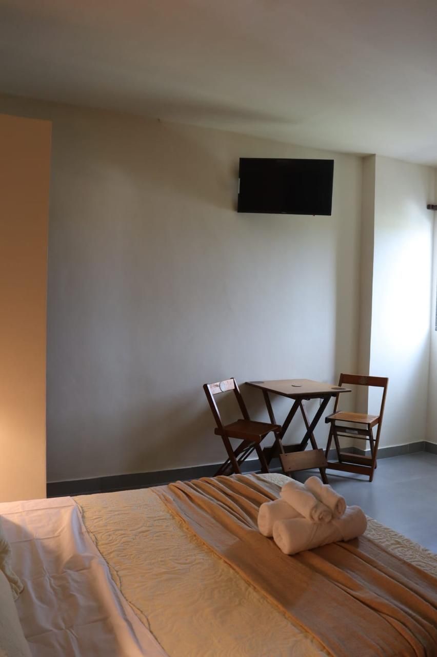 A hotel room with a bed, a small table with two chairs, a flat-screen TV mounted on the wall, and a window providing natural light.