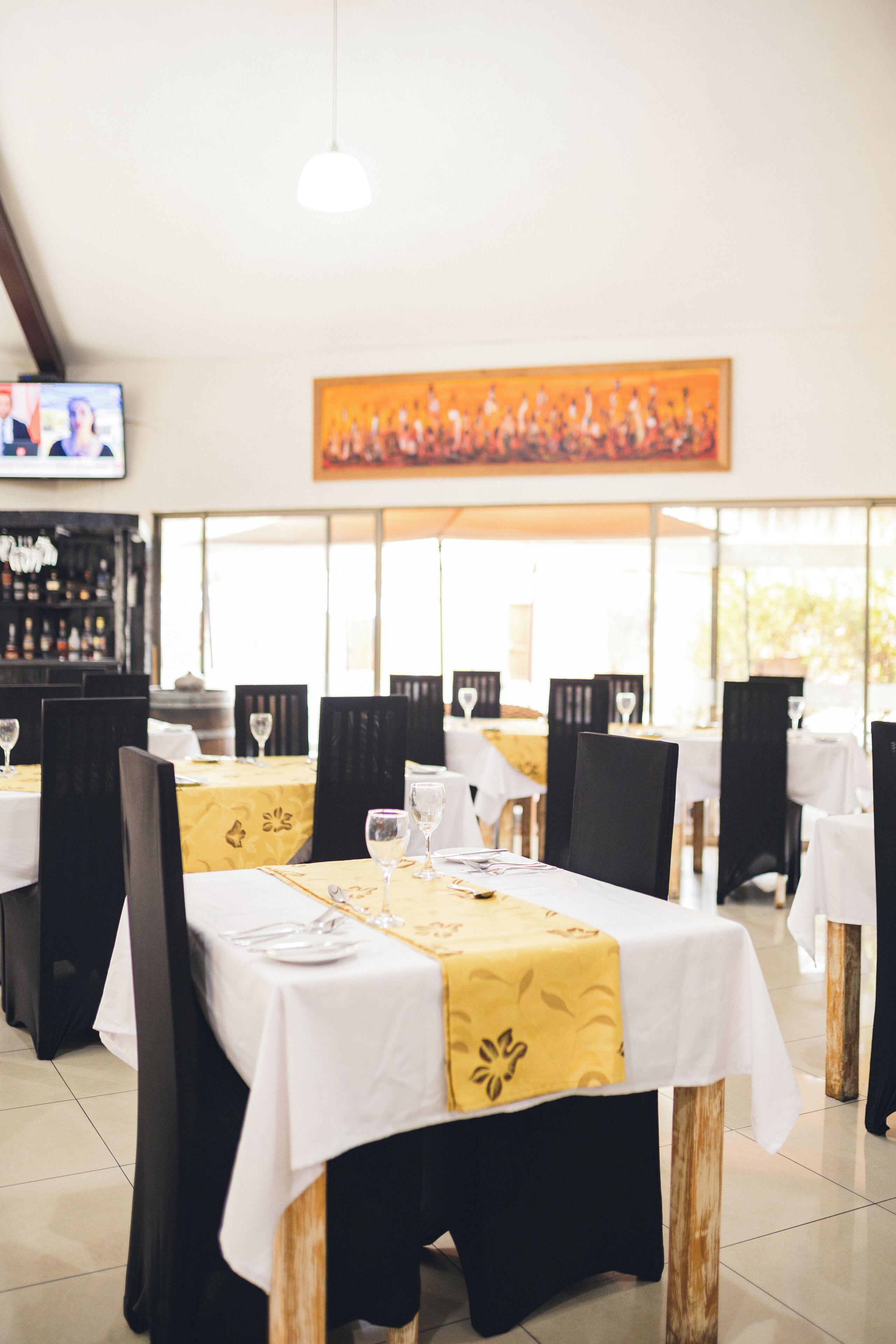 A restaurant with tables set for dining, a bar in the background, and a painting on the wall.