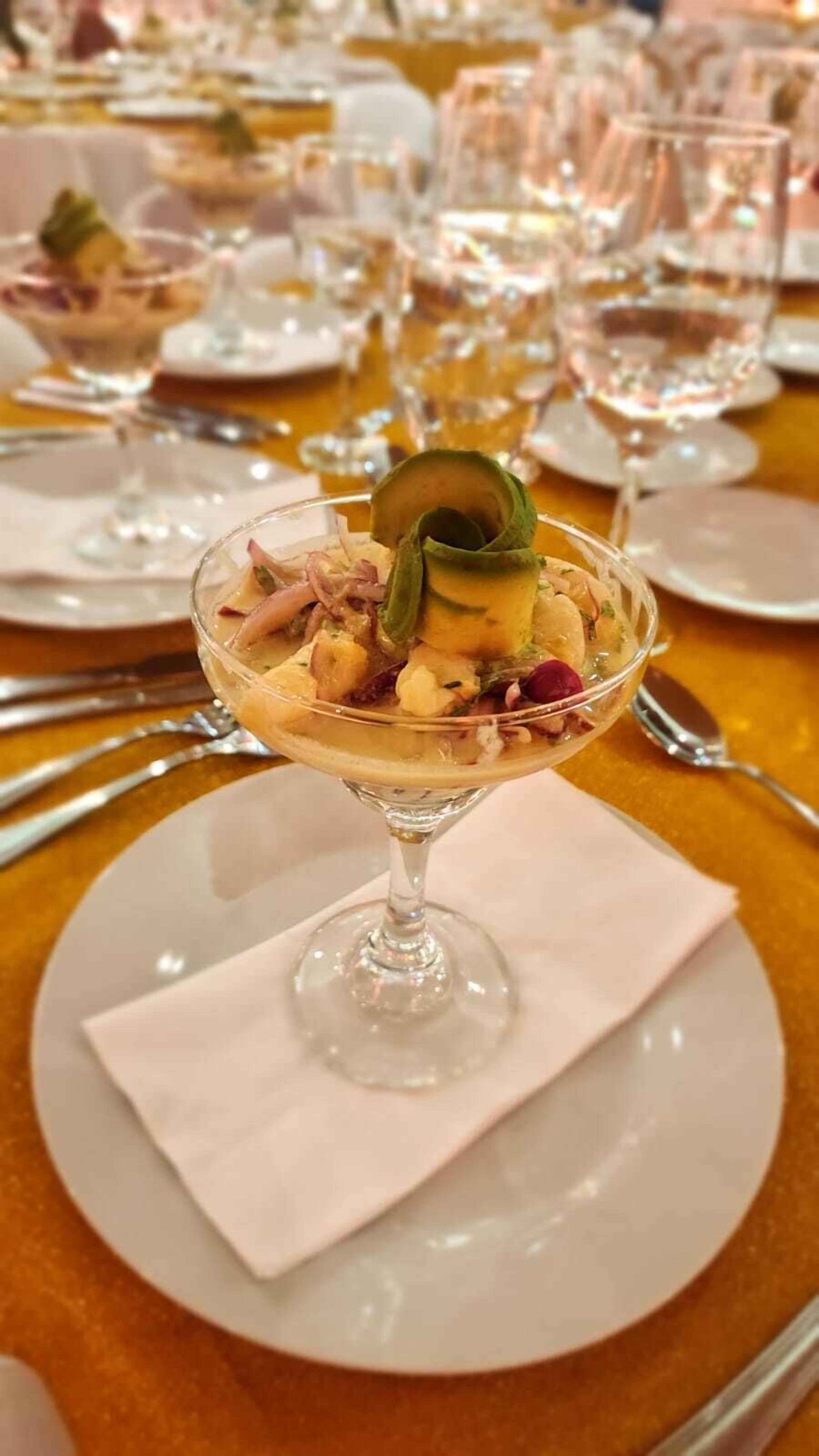 A dessert in a glass on a white plate with a napkin underneath, set on a table with other dishes and glasses.