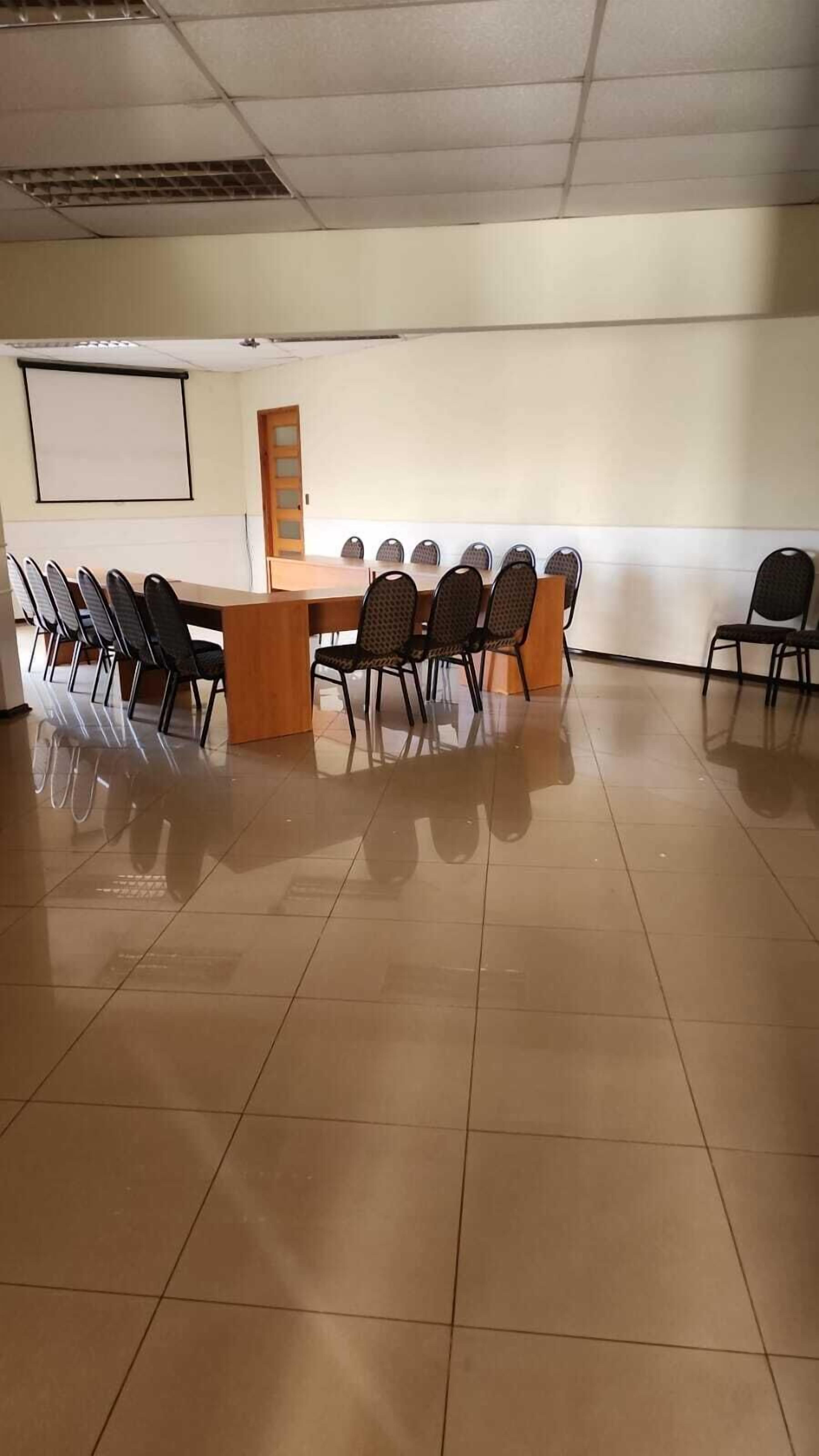 Un salón de conferencias con una larga mesa, sillas, una pantalla de proyector y una puerta.