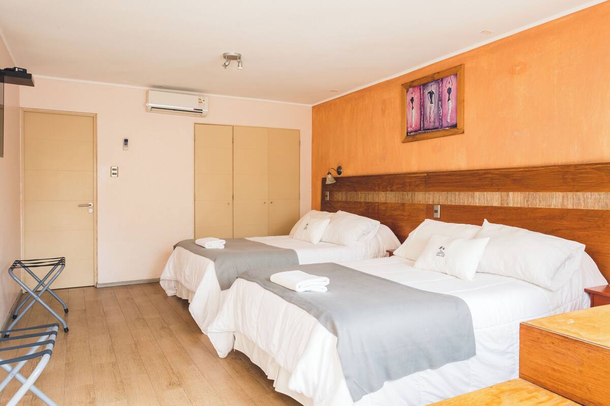 A hotel room with two beds, a wooden headboard, a wall-mounted air conditioner, and a small table.