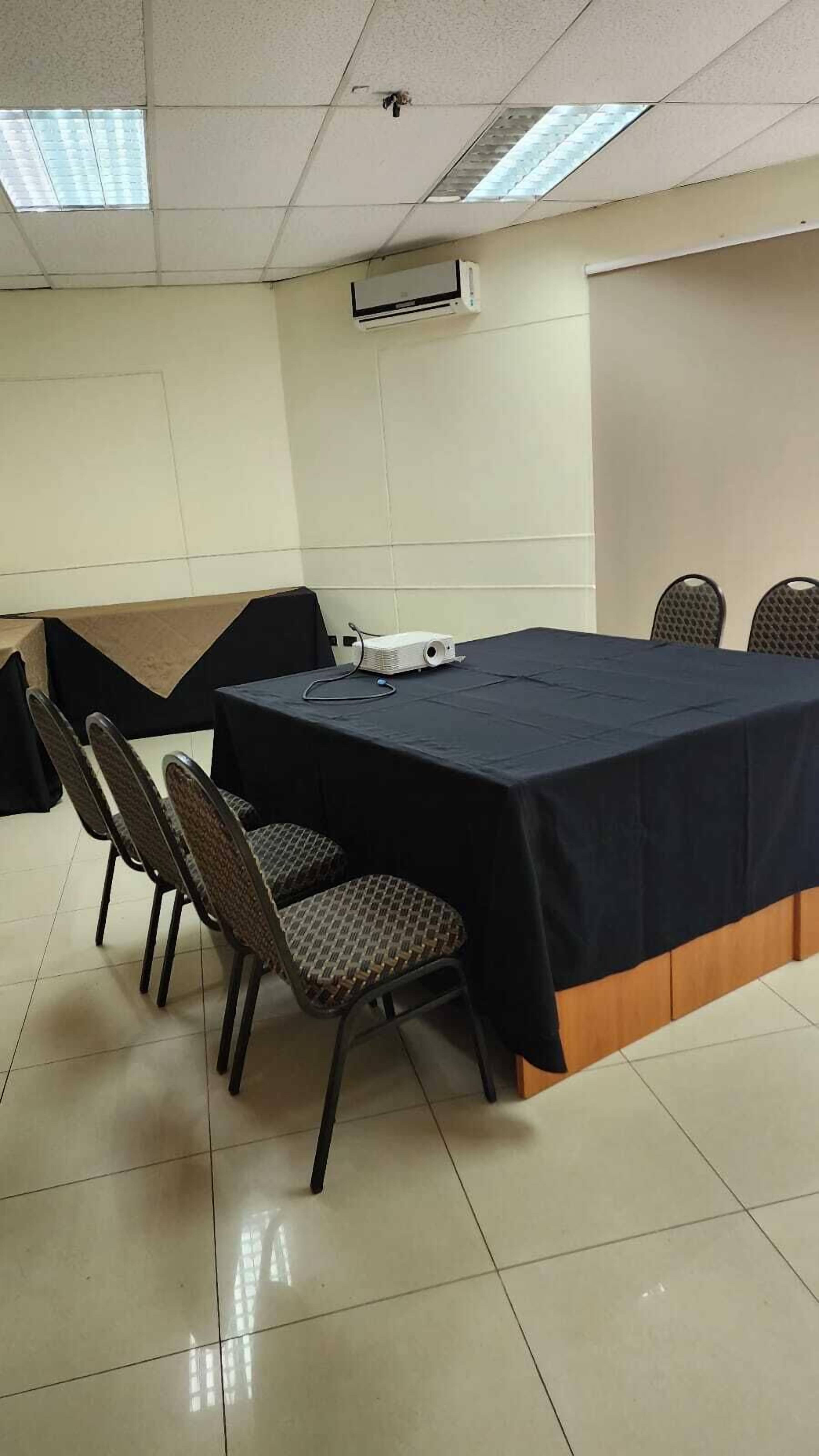 Un salón de conferencias con una mesa grande, sillas y un equipo de aire acondicionado en el techo.