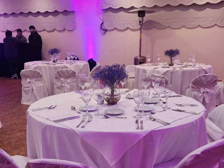 Ein Festsaal mit runden Tischen, gedeckt für eine festliche Veranstaltung, mit weißen Tischdecken und violetten Stühlen.