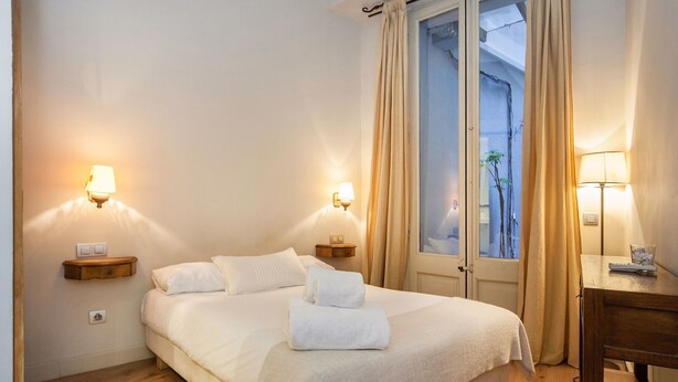 Ein Hotelzimmer mit einem Bett, zwei Nachttischen mit Lampen, einem Schreibtisch mit einer Lampe und Blick durch eine Glastür.