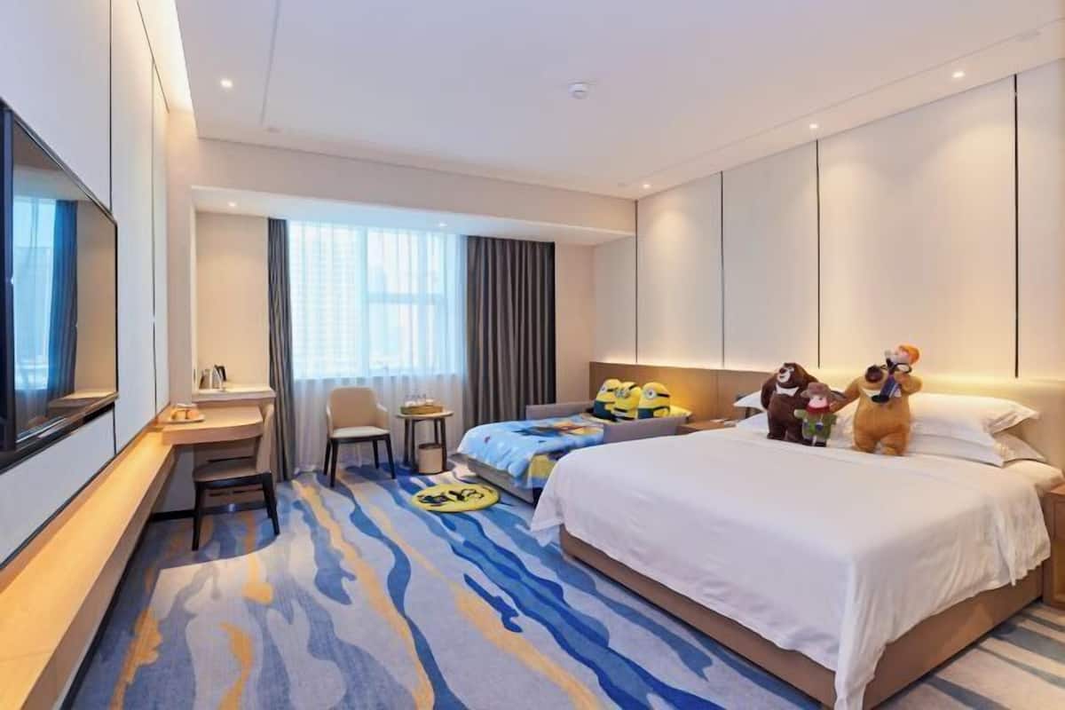 A hotel room with a bed, a desk, a chair, a small table, and a TV.