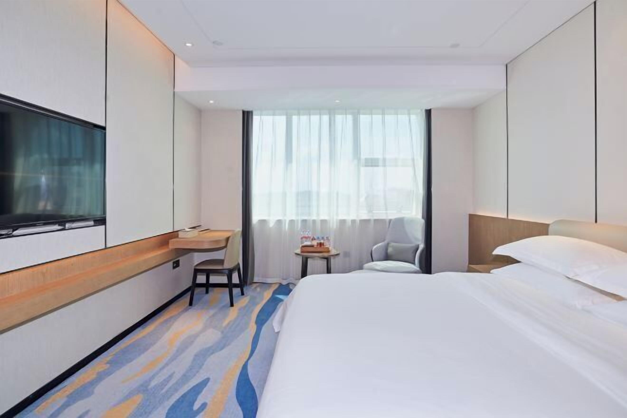 A hotel room with a bed, a desk, a chair, a TV, and a window with curtains.